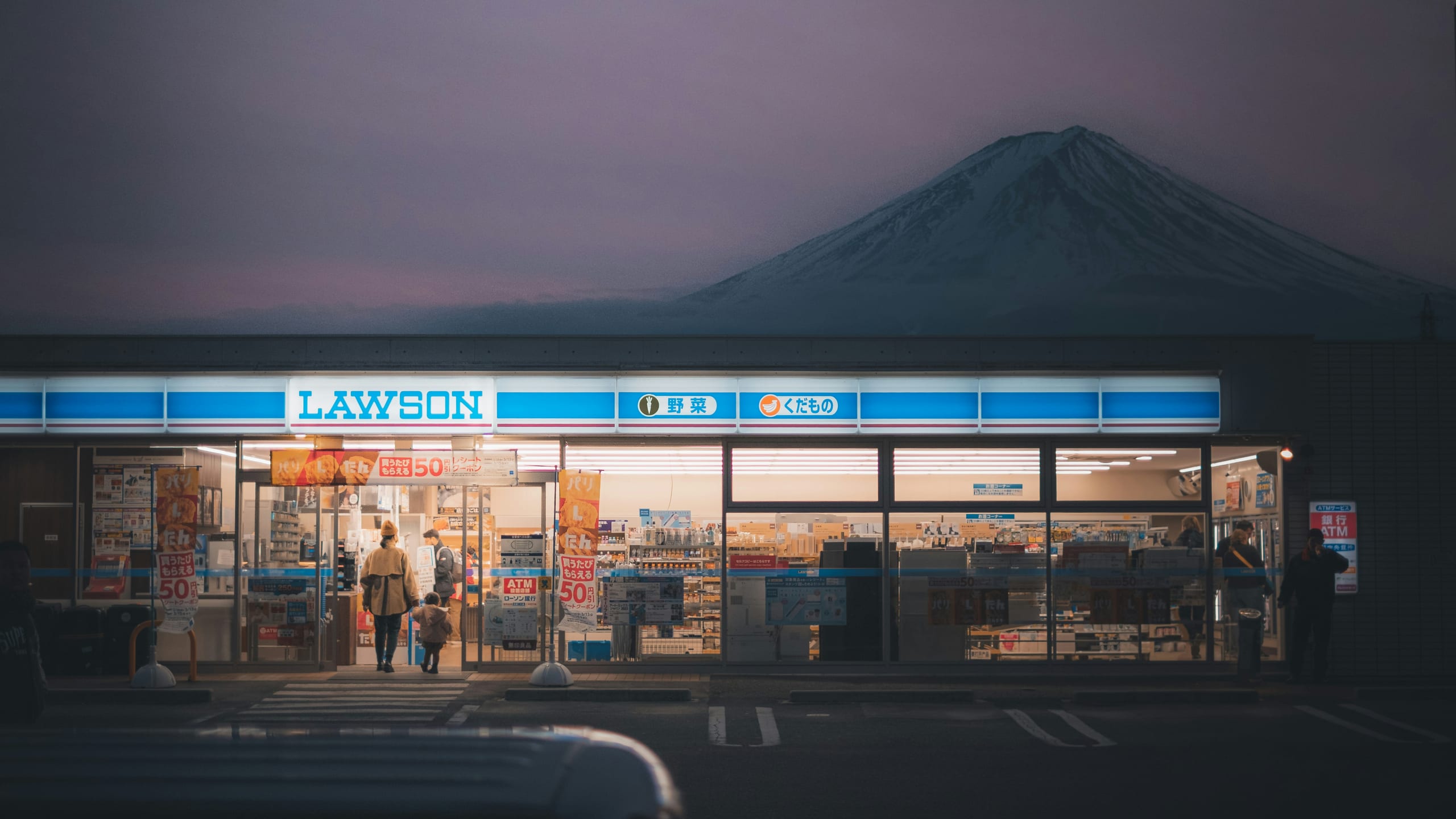 Mt. Fuji rising behind a Lawson convenience store at dusk